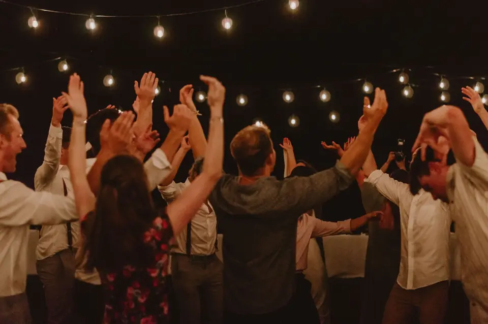 Guests with their arms up under string lights, late at night